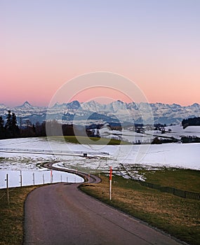 Pathway leading through winter hills on Gurten mountain with colorful evening sky and fameous jungfrau mountain range