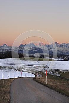 Pathway leading through winter hills on Gurten mountain with colorful evening sky and fameous jungfrau mountain range