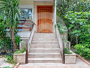 Pathway and stairs through the garden of a family house entrance with natural brown wood door.