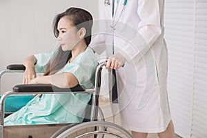 Patient asian woman paralysis is sitting in a wheelchair with doctor standing behind haul to her,Healthcare concept