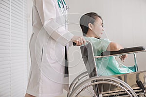 Patient asian woman paralysis is sitting in a wheelchair with doctor standing behind haul to her,Healthcare concept