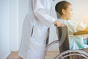 Patient asian women paralysis is sitting in a wheelchair with doctor standing behind haul to her,Healthcare concept