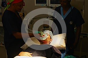 The patient is asleep now. a surgeon administering anesthetic to a patient before her surgery.