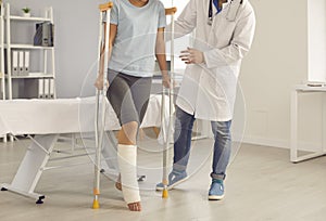 Patient with broken leg walking with crutches assisted by doctor during visit to hospital