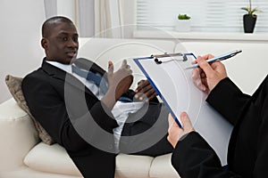 Patient On Couch And Psychiatrist Writing On Clipboard