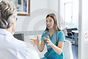 Patient with doctor in hospital waiting room discussing his symptoms. Young female doctor talking with her patient and explaining