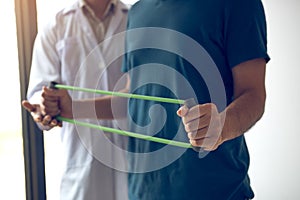 Patient doing stretching exercise with a flexible exercise band and a physical therapist hand to help in clinic room