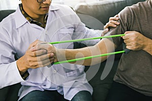 Patient doing stretching exercise with a flexible exercise band and a physical therapist hand to help in clinic room