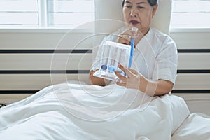 Patient elderly people woman using incentive spirometer or three balls for stimulate lung in bedroom