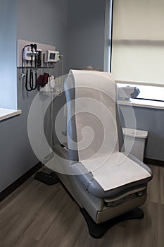 patient examination room with electric patient chair with hygiene paper roll and wall of medical tools and equipment with windows