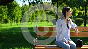 Patient girl looking at wristwatch waiting for friend sitting on bench in park