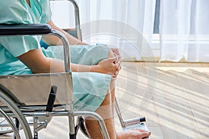 Patient having knee pain,sitting on wheelchair in the hospital room