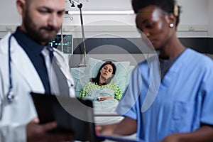 Patient on hospital bed feeling ill waiting for medic and nurse to read diagnosis from digtal tablet