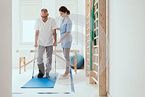 Patient in a leg brace exercising on a blue mat in a physiotherapy office