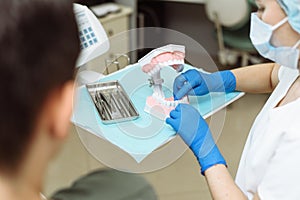 The patient looks at how to properly brush his teeth. The dentist shows clearly on the artificial jaw how to brush your teeth with