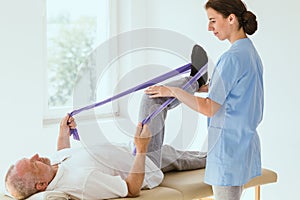 Patient lying on a physiotherapy bed and performing exercises with tapes under the care of a doctor