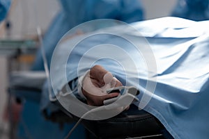 Patient lying on surgical bed wearing fingertip pulse oximeter in operating theatre