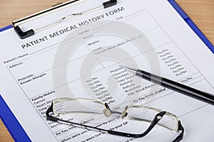 Patient medical history form on clipboard with pen and eyeglasses