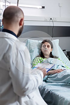 Patient with nasal cannula recieving oxygen in private ward looking at doctor presenting treatment options