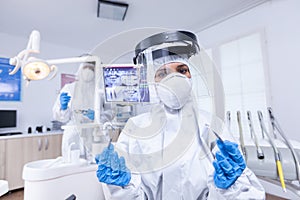 Patient pov of dentist in covid protectiv suit holding her tools