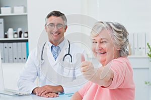 Patient showing thumbs up sign while sitting with doctor