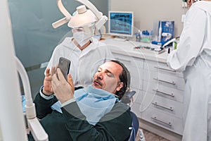 Patient using smartphone in dental office. Two female doctors preparing the procedure. concept of dental health and hygiene