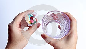 Patient woman holds medicine cup and a glass of water in hands, ready to take medicines with colorful pills, tablets and capsules