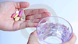 Patient woman holds medicine and a glass of water in hands, ready to take medicines with colorful pills, tablets and capsules.