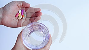 Patient woman holds medicine and a glass of water in hands, ready to take medicines with colorful pills, tablets and capsules.