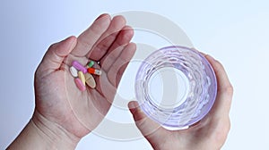Patient woman holds medicine and a glass of water in hands, ready to take medicines with colorful pills, tablets and capsules.