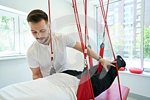 Patient working out on suspension trainer assisted by physiotherapist