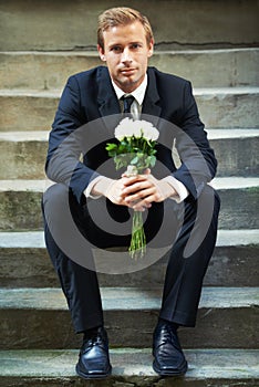 Patiently waiting for love. A handsome man wearing a suit and sitting on stairs holding a bunch of white roses.