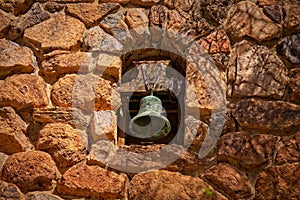 A patinated mission bell set in an old stone wall.