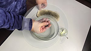 Patination of copper coins with sulfuric ointment. A man rubs a coin with sulfuric ointment in hot water