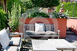 Patio tucked away in a beautiful garden corner with red-painted walls, flowering plants and cozy benches with cushions.