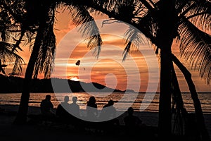 Patong beach in phuket during the sunset with six persons sit near the sea and palm trees