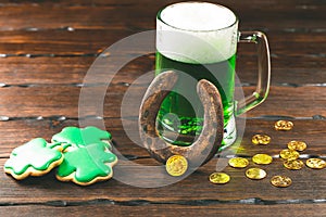 Patrick`s day background with a Glass of green beer and clover gingerbread with gold coins on wooden