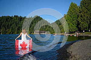 Patriot woman standing in the mazarine color water of the Cultus Lake and holding up a Canadian flag