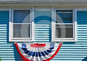 Patriotic bunting displayed beneath two wood windows on a blue painte house for Memorial Day or the 4th of July USA