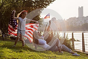 Patriotic holiday. Happy family, mother and daughter with American flag outdoors on sunset. USA celebrate independence