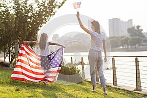 Patriotic holiday. Happy family, mother and daughter with American flag outdoors on sunset. USA celebrate independence