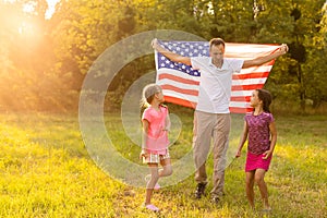 Patriotic holiday. Happy family, mother and daughters with American flag outdoors on sunset. USA celebrate independence