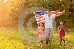 Patriotic holiday. Happy family, mother and daughters with American flag outdoors on sunset. USA celebrate independence