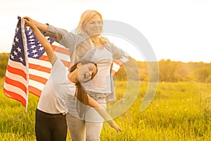 Patriotic holiday. Happy family, mother and her daughter child girl with American flag outdoors. USA celebrate 4th of