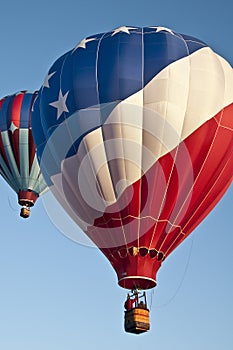 Patriotic red white and blue hot-air balloon taking off with many other hot air balloons into the blue morning sky