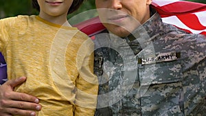 Patriotic soldier hugging his little son wrapped in US flag, peace for family