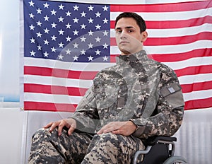 Patriotic soldier sitting on wheel chair against american flag