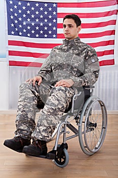 Patriotic soldier sitting on wheel chair against american flag