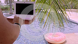 Pattaya, Thailand - May 15, 2019: Male working on his laptop, sitting by the pool. Male hands on the keyboard in the
