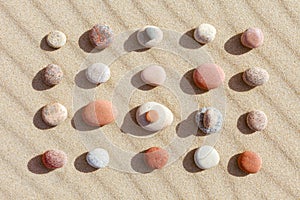 Pattern of colored pebbles on clean sand. Flat lay, top view